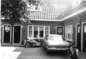 De invalide mw. Sloos weigert de huurverhoging te betalen vanwege de slechte toestand van haar woning aan de Transvaalhof. Pas als zij door de vloer zakt wordt er gerepareerd. Op de foto: Transvaalhof 31 met de invalidenwagen van mw. Sloos 31 mei 1975